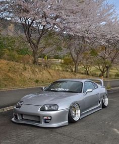 a silver car parked on the side of a road next to trees with pink flowers