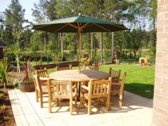 a wooden table with chairs and an umbrella in the middle of a patio area outside