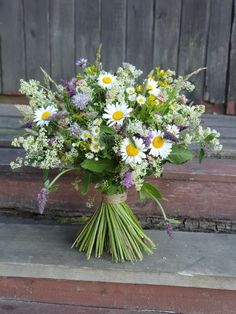 a bouquet of wildflowers and daisies sits on the steps in front of a wooden door