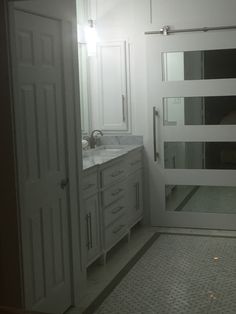 a white bathroom with double sinks and large mirrors on the wall, along with an open door leading to another room