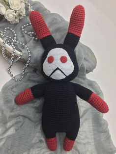 a crocheted black and red stuffed animal laying next to a flower on a bed