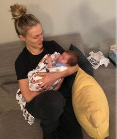 a woman holding a baby on top of a couch next to a yellow bean bag