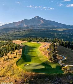 an aerial view of a golf course with mountains in the background and trees on either side