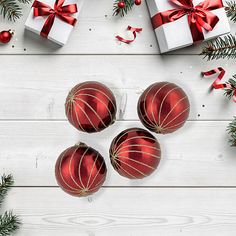 three red christmas balls with ribbons and bows on white wood background surrounded by evergreen branches