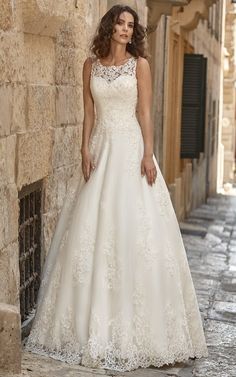 a woman in a white wedding dress standing on the side of an alleyway with stone buildings and cobblestone streets