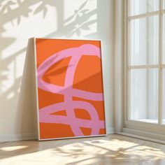 an orange and pink painting sitting on top of a wooden floor next to a window