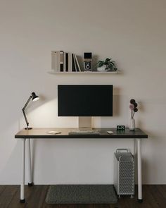 a desk with a computer monitor and keyboard on it in front of a white wall