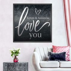 a black and white love you sign in a living room with pink curtains, a chair and a table