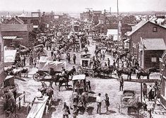 an old black and white photo of a town with horses, wagons and people in it