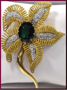 "The captivating flower brooch has a center oval shaped 10.00 ct deep forest green tourmaline. It dates from the 1960's. It is surrounded by 4 gold coiled leaves encrusted with 1.75 ct of round diamonds in the center of each leaf. It all gracefully blooms out of the golden stem. This is enticing appeal all swathed up into a pin. The pin weighs 45 grams. It measures 2 ½ \" long and 2\" wide at its widest point. P 518S SIX MONTH LAY-AWAY AVAILABLE - PLEASE CONTACT ME TO SET UP A PLAN" Luxury Green Brooch For Formal Occasions, Elegant Green Flower Brooches, Elegant Green Oval Brooches, Green Oval Brooches For Formal Occasions, Brooch Diamond, Brooch Flower, Bouquet Gift, Bouquet Bridal, Floral Brooch