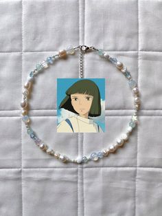 a necklace with a picture of an anime character hanging from it's side on a white quilt