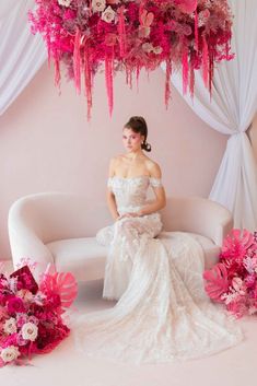 a woman in a wedding dress sitting on a couch with pink flowers hanging from the ceiling