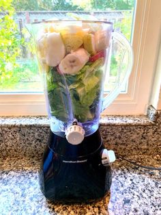 a blender filled with fruit and vegetables on top of a counter next to a window