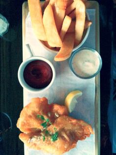 a wooden tray topped with fried food next to fries and dipping sauces on top of it