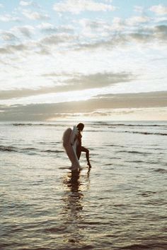 a man standing in the ocean with his surfboard under his arm as he wades into the water