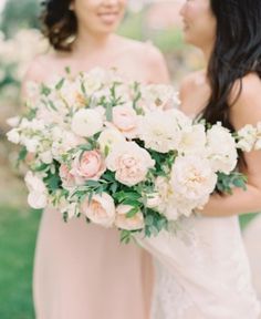 two bridesmaids holding bouquets of flowers in their hands and looking into each other's eyes