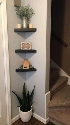 three shelves with plants and candles on them in the corner of a room next to stairs