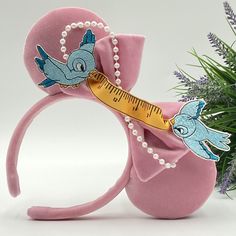 a pink mouse ears with blue birds on it and a measuring tape around the ears