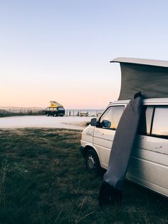 a white van parked on top of a lush green field next to the ocean with a covered roof