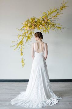 a woman standing in front of a white wall wearing a wedding dress with yellow flowers on it