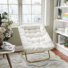 a white chair sitting in front of a window next to a table with flowers on it