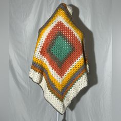 a crocheted blanket on a stand with white fabric behind it and grey background