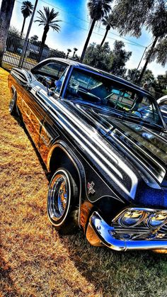 an old car is parked on the grass in front of palm trees and other cars