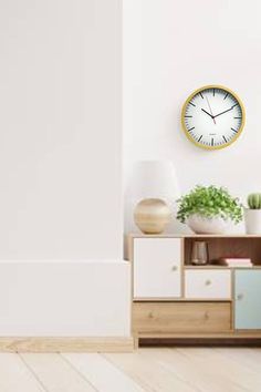 a white wall with a clock on it and some plants in the corner next to it