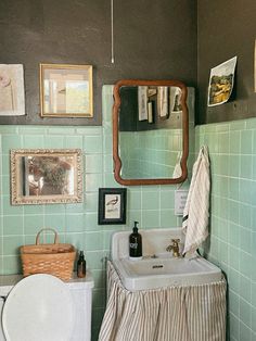 a bathroom with green tiles and pictures on the wall above the sink, toilet and mirror