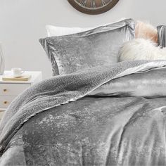 a bed with silver sheets and pillows next to a clock