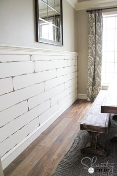 a wooden table sitting in front of a window next to a wall with a mirror on it