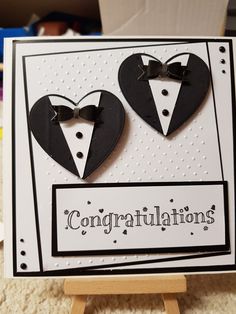 congratulations card with two black hearts and bow ties on it's chest, in front of a cardboard easel