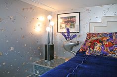 a bed with blue sheets and pillows in a room that has flowers on the wall