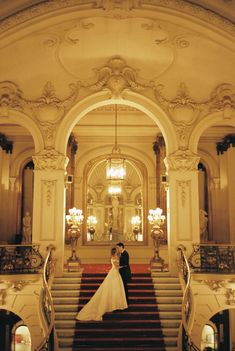 a bride and groom are standing on the stairs in an ornately decorated building with chandeliers