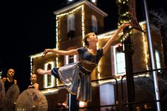 a woman is dancing in front of a building with christmas lights on it and an umbrella