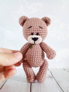 a small crocheted teddy bear sitting on top of a wooden table next to a person's hand