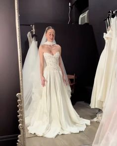 a woman standing in front of a mirror wearing a wedding dress