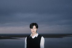 a man standing in front of a body of water under a dark sky with clouds