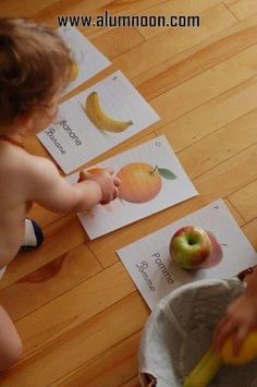 two toddlers playing with apples and bananas on the floor in front of their matching cards