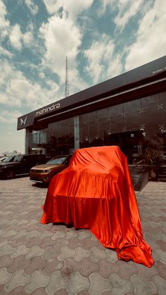 a car covered in an orange cloth sits on the ground next to a building with a sky background