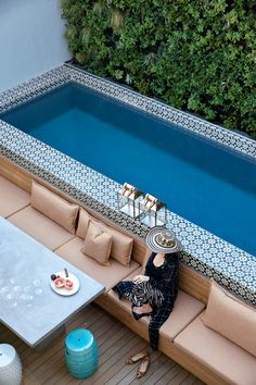 a woman sitting on a couch next to a pool in the middle of a patio