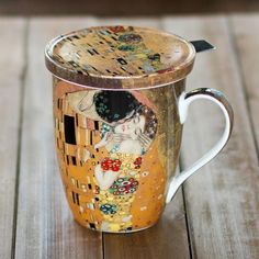 a coffee cup with an artistic painting on the side and lid sitting on a wooden table