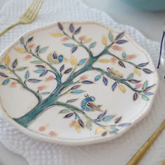 a plate with a tree painted on it next to gold utensils and silverware