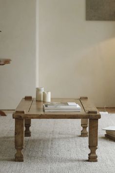 a coffee table with two candles and books on it in front of a white wall