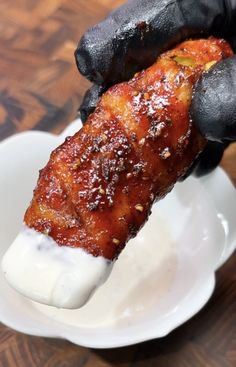 a person in black gloves is dipping sauce on a piece of meat into a white bowl