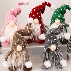 four knitted gnomes sitting next to each other on a white surface with christmas trees in the background