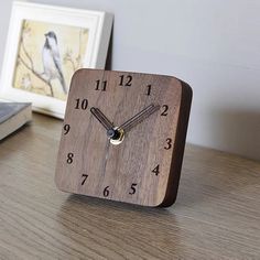 a small wooden clock sitting on top of a desk next to a laptop and framed pictures