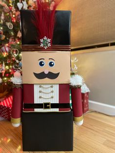 a nutcracker made out of cardboard sitting on top of a wooden floor next to a christmas tree