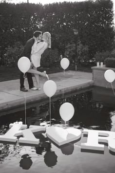 a couple kissing in front of balloons floating on the water at their wedding reception, black and white photo