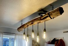 some light bulbs hanging from a wooden beam in a room with white curtains and windows